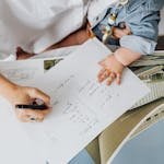 A mother works on a project with a baby on her lap at a home workspace.